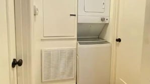 Une petite buanderie équipée d’un lave-linge et d’un sèche-linge encastrés, d’une bouche d’aération et d’une porte dotée d’une poignée ronde.