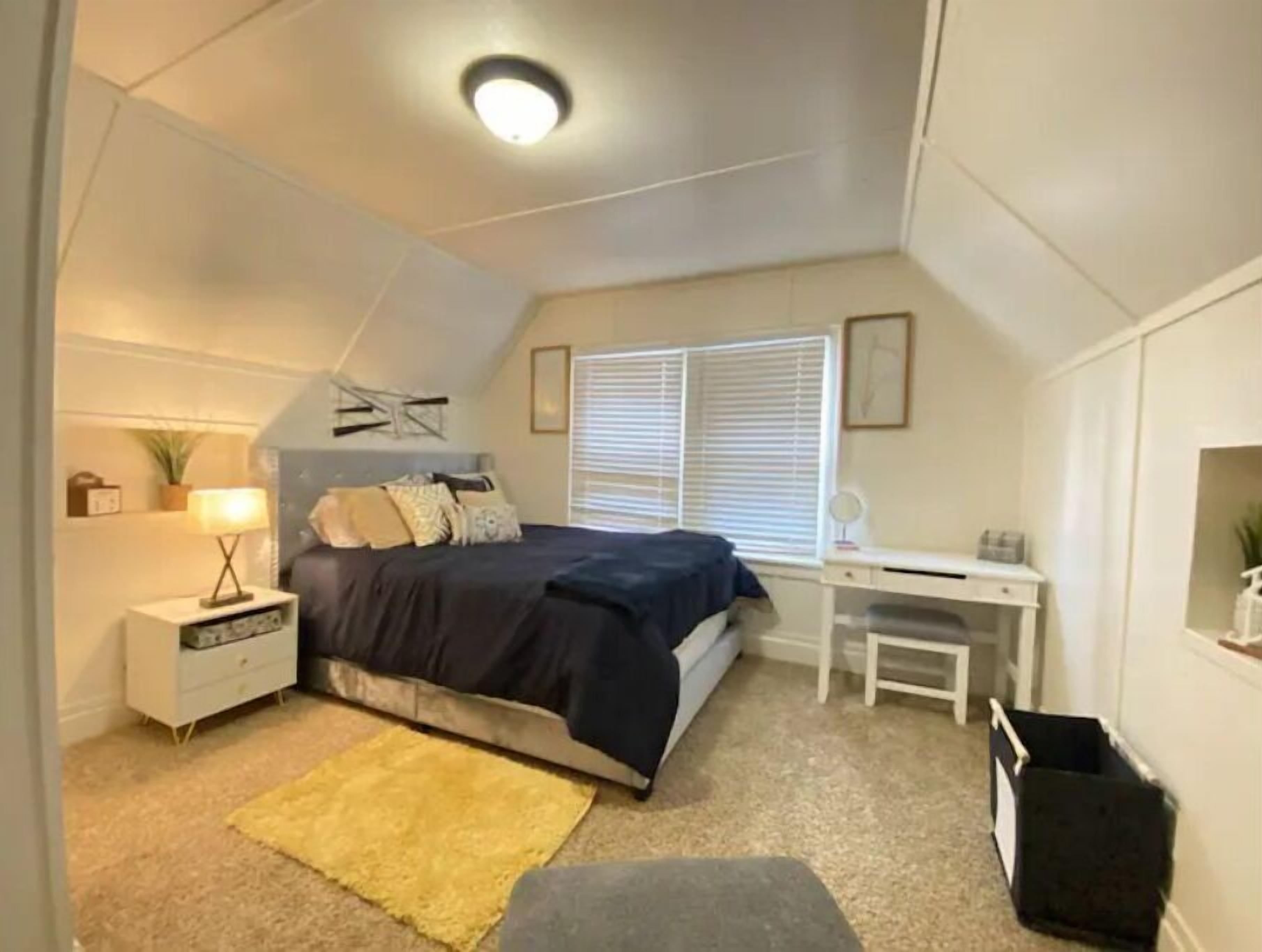 A bedroom with a bed, desk, and a small window.