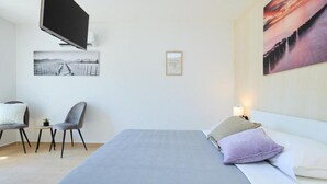 Ein Hotelzimmer mit Bett, Fernseher an der Wand, einem Sessel und einem kleinen Tisch.