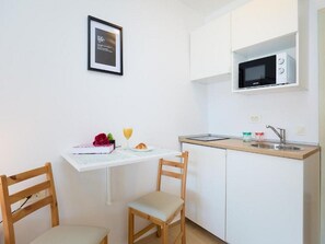 A small kitchenette with a microwave, sink, and a table with chairs. There is a framed picture on the wall and a glass of orange juice on the table. - Palm Tree Apartments - Studio Apartment with queen bed (A6) (Dubrovnik)