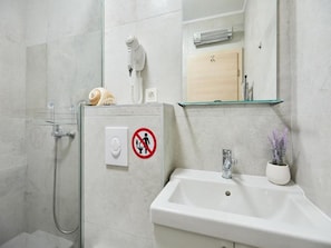 A bathroom with a shower, a sink, a hairdryer, and a no-entry sign.