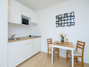 A compact kitchen with white cabinets, a microwave, and a sink. There is a dining table with two chairs and a vase with flowers.