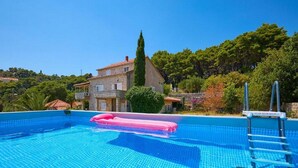 A swimming pool with a pink float, a ladder, and a stone building in the background. - Palm Tree Apartments - A8 (Dubrovnik)