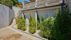 A two-story house with a stone balcony, a covered staircase, and a garden with shrubs. - Palm Tree Apartments - A8 (Dubrovnik)