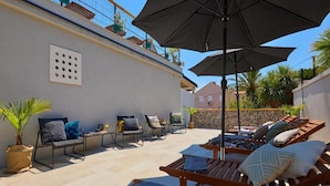 An outdoor patio with lounge chairs, umbrellas, and potted plants.