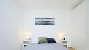 A modern bedroom with a bed, two bedside tables, a nightstand, a wall-mounted picture, and a wardrobe.