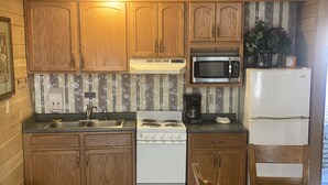Cocina compacta con armarios de madera, estufa, microondas y refrigerador.
