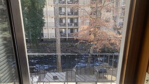 Ein Balkon mit einem Metalltisch und Stühlen, mit Blick auf einen Fluss und ein Gebäude mit Balkonen.