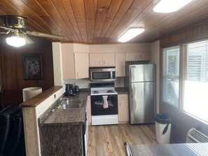 Cocina compacta con techo de madera, microondas empotrado, refrigerador de acero inoxidable y ventana con persianas.