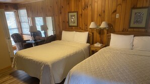 Ein Zimmer mit zwei Betten, Holzwänden, einem Schreibtisch mit Stuhl und einem Fenster mit Jalousien.