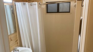 Een kleine badkamer met een houten plafond, een wit wastafelmeubel, toilet en bad.