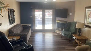 Een woonkamer met een plafondventilator, een open haard, een bank, een fauteuil en een televisie.