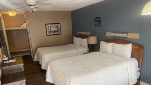 Een hotelkamer met twee extra bedden, een bureau, een stoel, een kledingkast en een plafondventilator.