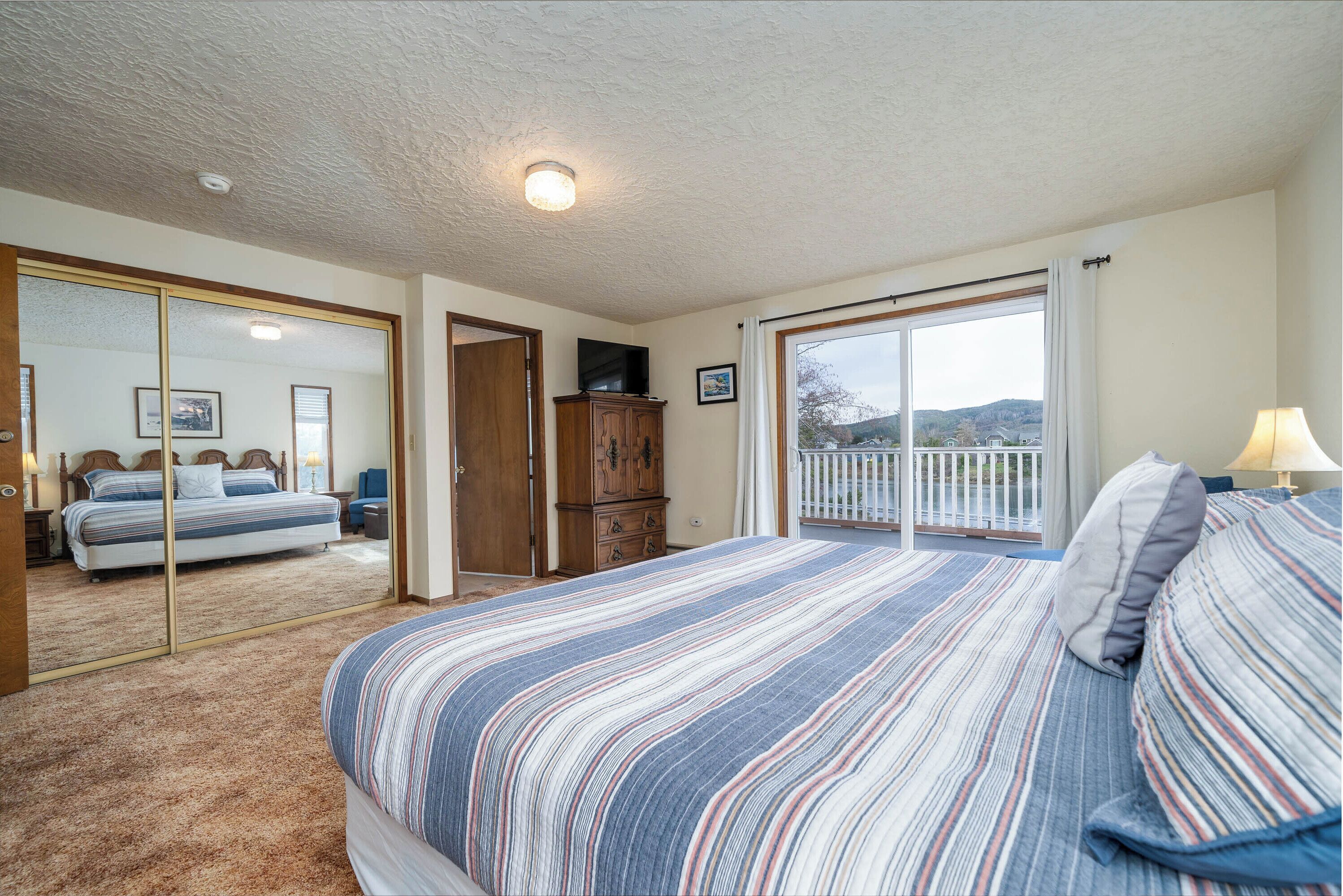 A bedroom with a large bed, a wardrobe, a television, and a balcony with a view.