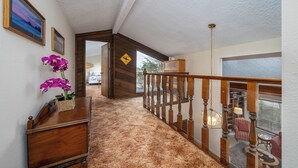 Ein Flur mit einer Holztreppe, einem Holztisch mit einem Blumenkorb und Blick ins Freie.