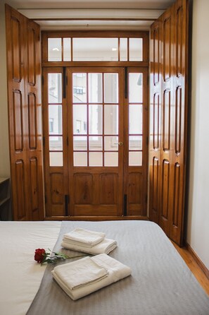 A hotel room with a large wooden door, a bed with a grey bedspread, and two folded white towels. - Porto Brasil Hostel (Porto)