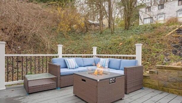Une terrasse extérieure avec un ensemble de meubles de jardin en rotin brun, une table basse avec un plateau en verre et un foyer.