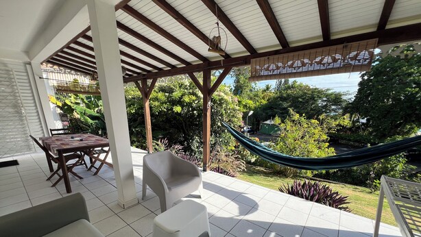 Une terrasse couverte avec une table et des chaises, un hamac et une vue sur la verdure environnante.