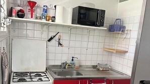 Une cuisine équipée d’une cuisinière à gaz, d’un four à micro-ondes et d’un évier. On y trouve des placards, une étagère avec des ustensiles de cuisine et une fenêtre au-dessus de l’évier.