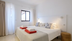 A hotel room with a bed, curtains, a window, and a bedside lamp. - Casa Carbo, Air Conditioning - Puerto del Carmen, Lanzarote (Puerto del Carmen)