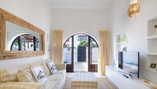 A living room with a sofa, ottoman, TV, and a large mirror. - Casa Carbo, Air Conditioning - Puerto del Carmen, Lanzarote (Puerto del Carmen)