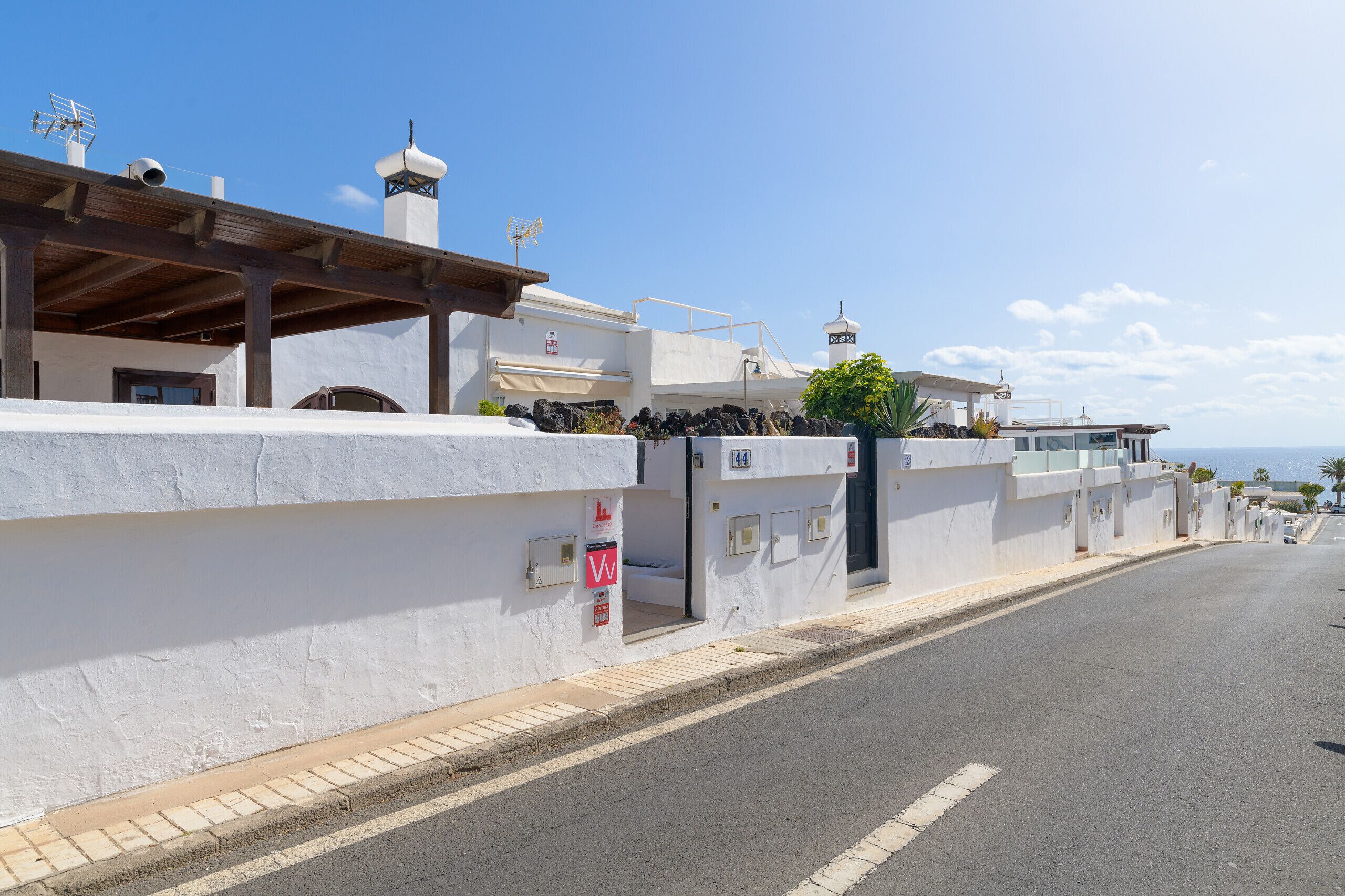 Una calle costera con edificios blancos, cielo despejado y vista al mar.