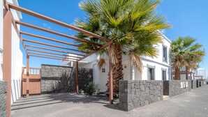A white building with a stone wall, a wooden gate, and palm trees. - Casa LAGO (Playa Blanca)