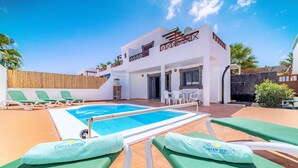 A pool area with lounge chairs and a building with a name sign. - Casa LAGO (Playa Blanca)