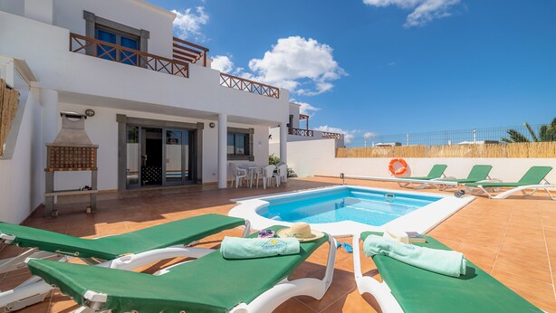 A poolside area with lounge chairs, a pool, and a two-story building with a balcony. - Casa LAGO (Playa Blanca)