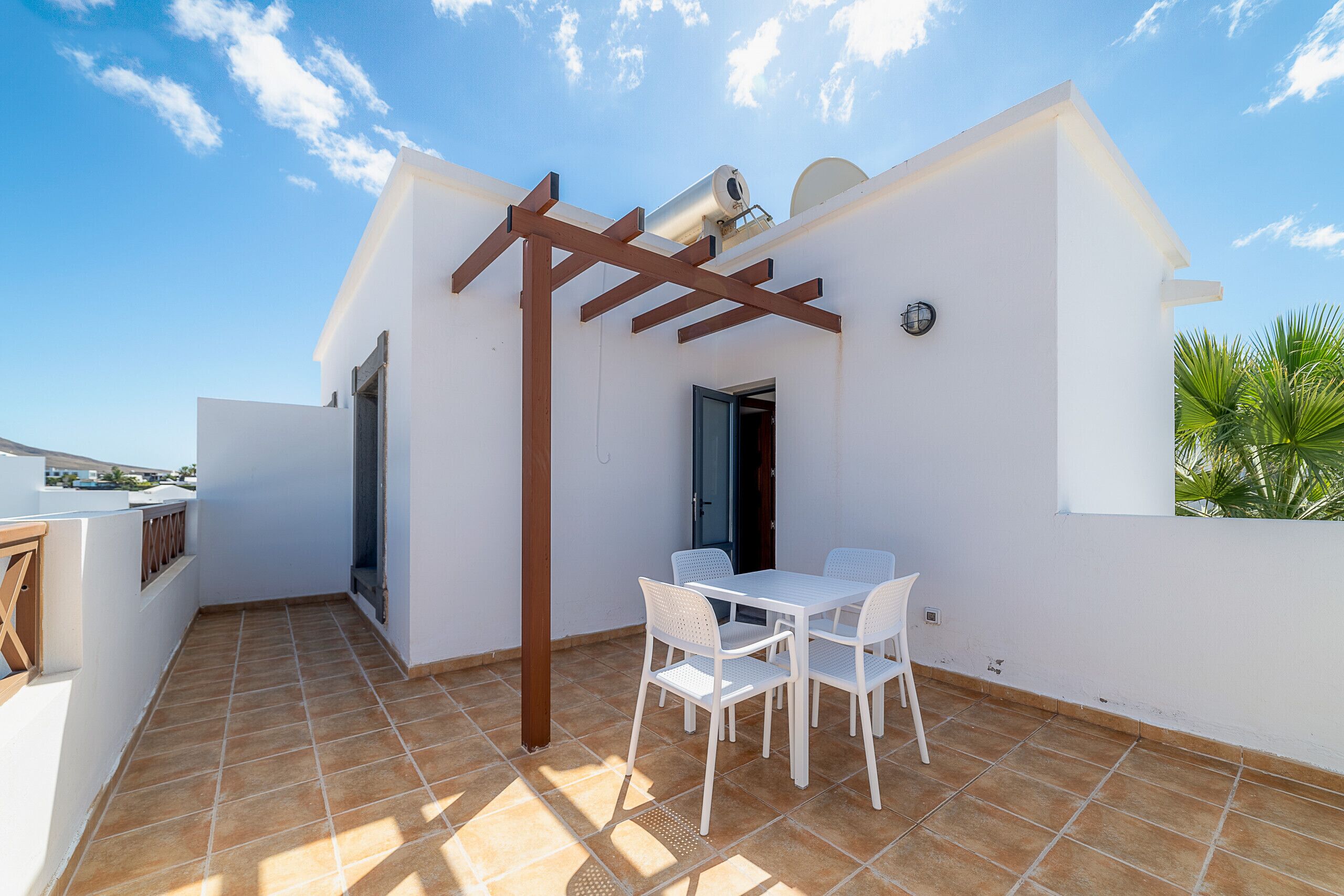 Une terrasse sur le toit avec une table et des chaises blanches, une pergola et une vue sur le ciel.