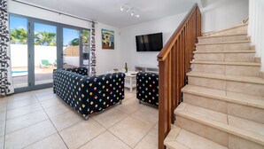 A spacious living area with a staircase, a flat-screen TV, and a pool visible through the glass doors. - Casa LAGO (Playa Blanca)