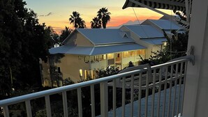A balcony with a metal railing overlooking a residential area during sunset. - Studio Hibiscus n°2 with sea and mountain views, beach access, + cistern (Le Gosier)