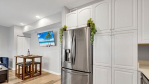 A modern kitchen with white cabinetry, a stainless steel refrigerator, and a wooden dining table with two chairs. - Wellington Garden (West Palm Beach)