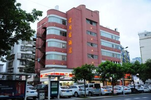 Un hotel de varios pisos con fachada roja, varios balcones y una fila de coches estacionados al frente.