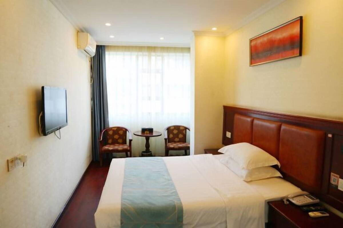 Une chambre d’hôtel avec un lit, une télévision, deux chaises, une petite table et un tableau au mur.