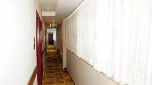 A hotel corridor with a patterned carpet, red doors, and white curtains.