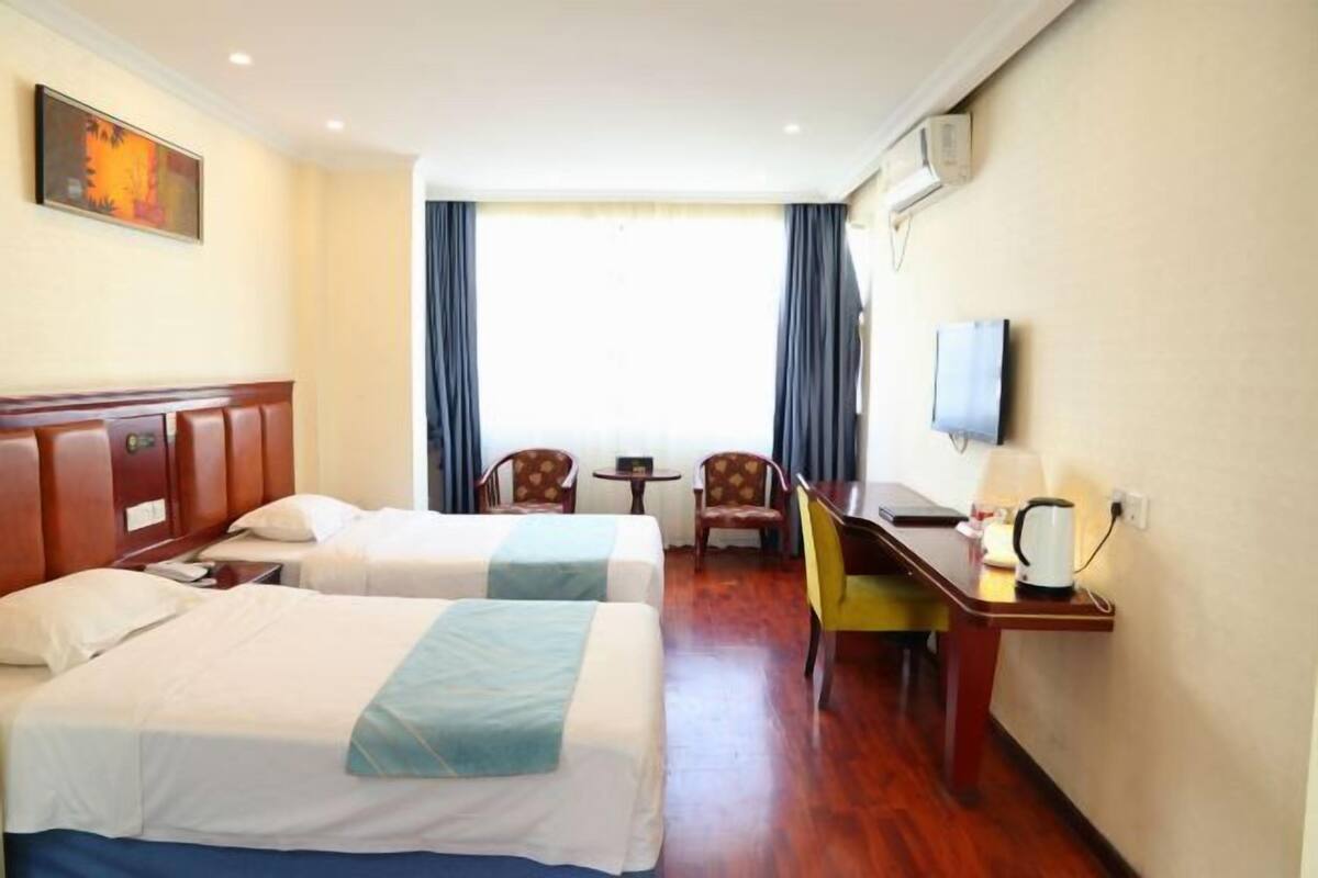 Une chambre d’hôtel avec deux lits, un bureau, une chaise, une télévision et une fenêtre avec des rideaux.
