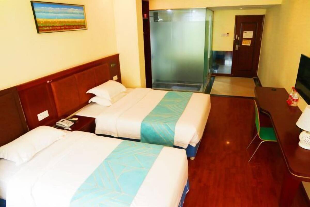 Une chambre d’hôtel avec deux lits, un bureau, une chaise, une télévision et une douche en cabine de verre.