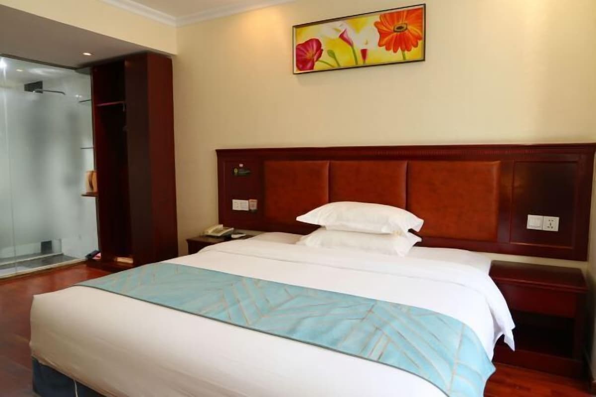 Habitación de hotel con una cama grande, cabecera de madera, mesita de noche y zona de ducha.