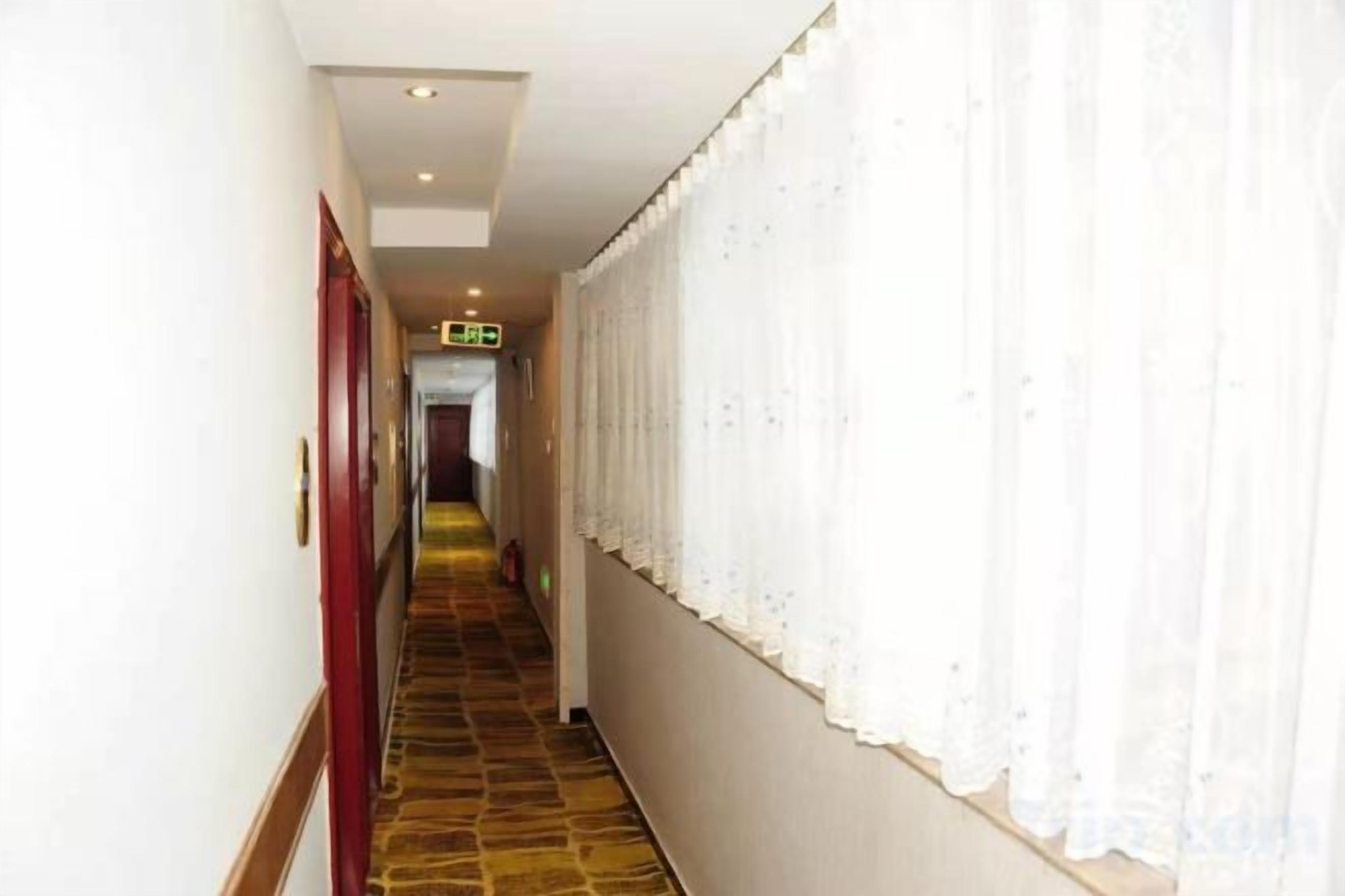 A hotel corridor with a carpeted floor, white walls, and a red door on the left.