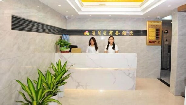 A hotel reception area with a marble counter, two receptionists, a plant, and a sign above the counter. - Xingyuexing Hotel (Zhuhai Gongbei Port) (Zhuhai)