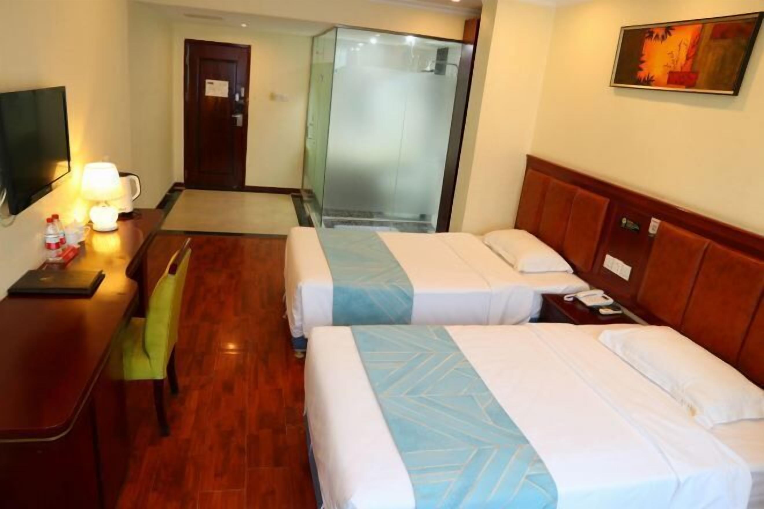 Une chambre d’hôtel avec deux lits, un bureau avec une lampe, une télévision et un espace douche.
