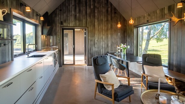A modern kitchen with a large window, wooden walls, and a dining area with chairs and a table.