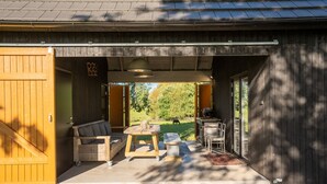 A covered outdoor seating area with a table and chairs, a wooden bench, and a grill.