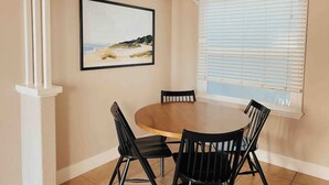 A dining area with a round table and four chairs, a framed picture on the wall, and a window with blinds. - Back Unit · Beach House in the <3 of Balboa Peninsula (Newport Beach)