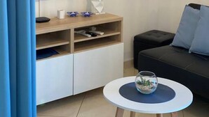 En moderne stue med et fladskærms-tv, et træunderholdningsmøbel, et rundt sofabord med en glas skål, en sort sofa og en hængende lampe.