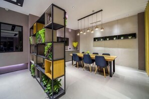 A modern dining area with a wooden table, black chairs, and a tall shelving unit with plants. - Homeinn Hotel (Yangzhou University Grand Canal Museum) (Yangzhou)