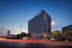 Un hôtel à plusieurs étages, doté d’un design moderne, avec une entrée imposante et un espace de stationnement bien visible.