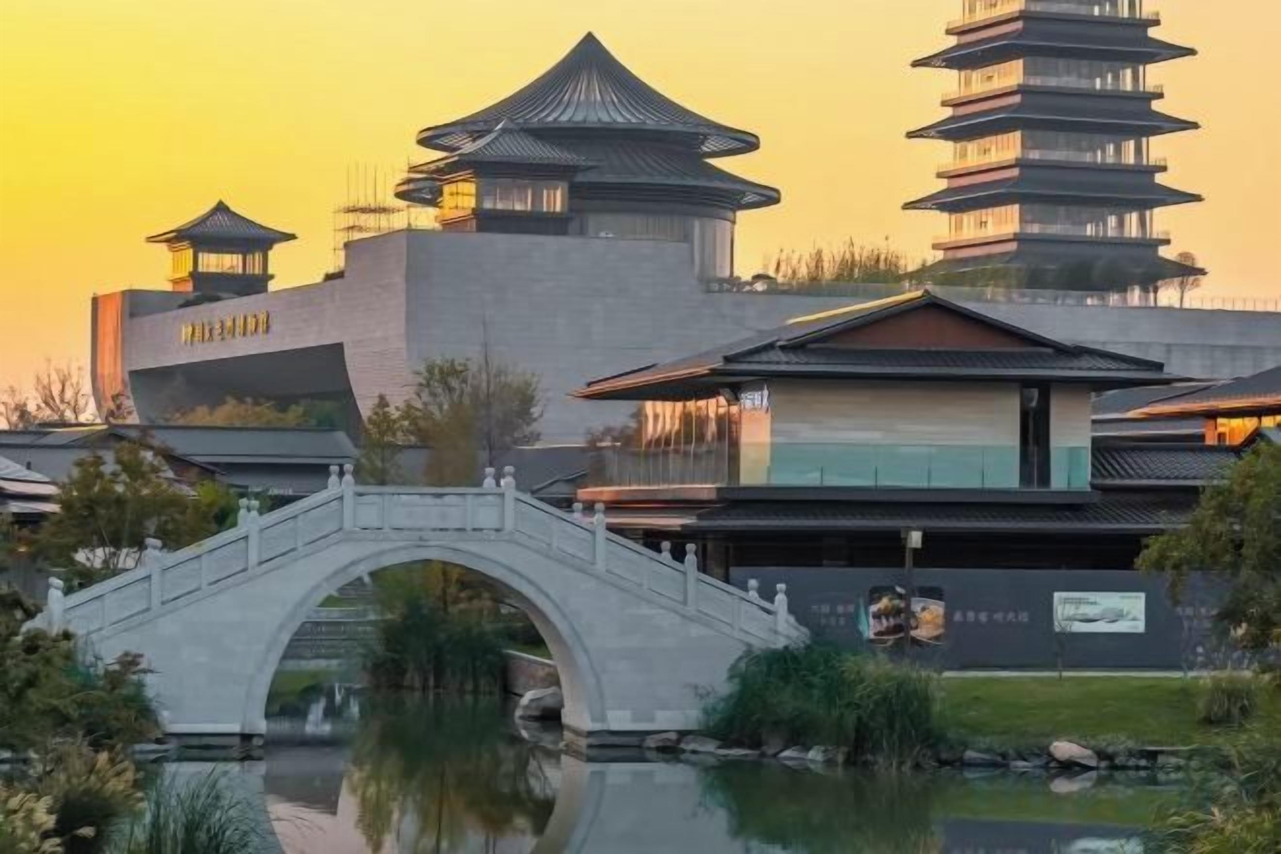 A traditional building with a pagoda-style roof, a stone bridge, and a reflection in the water.