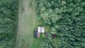 Une vue aérienne d’une petite maison à un seul étage, dotée d’un toit recouvert de panneaux solaires, et entourée d’une forêt dense.